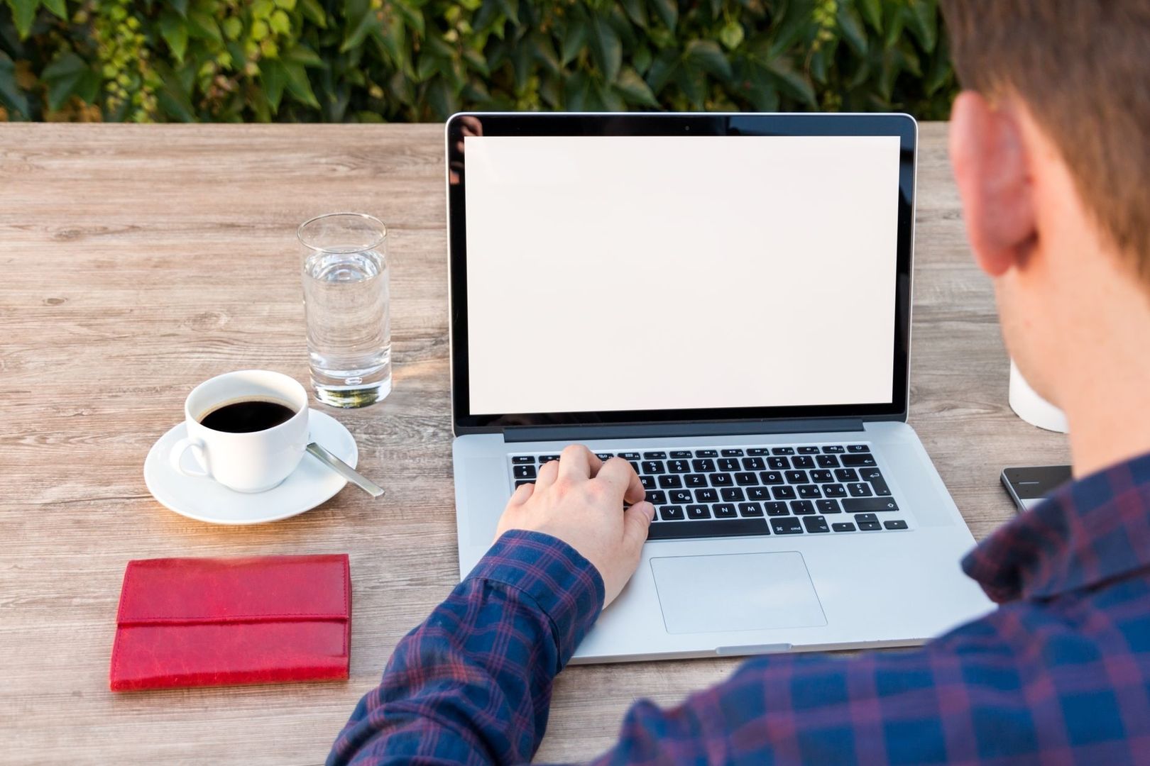 Person arbetar vid en laptop utomhus, med kaffe och vatten på bordet